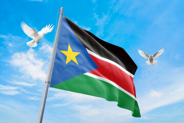 Waving flag of South Sudan in beautiful sky and flying pigeons. South Sudan flag for independence day. The symbol of the state on wavy fabric.