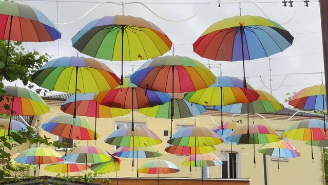 Lots of multi-colored rainbow umbrellas hang above city street. Fun lgbt coming out concept. Colorful gay symbol. Urban art overhead decoration. Many vivid parasols sway open air. Blue sky background.