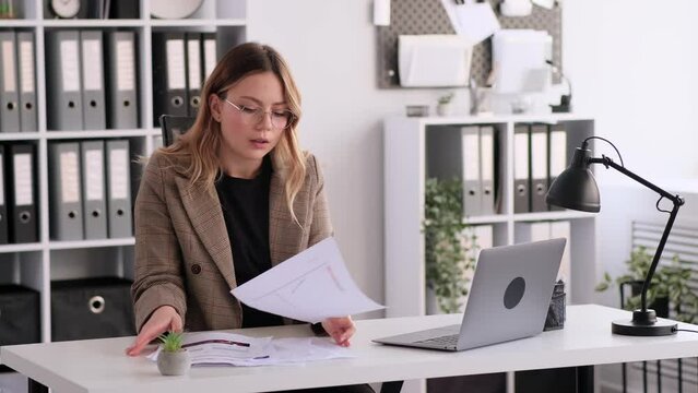 Concentrated Caucasian woman working with papers and laptop in office. Professional entrepreneur engaged in business accounting or planning project.