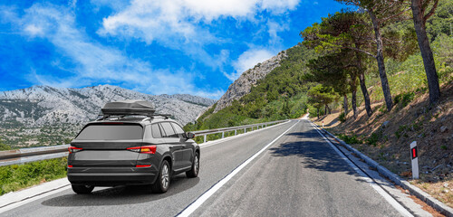 Travel car drives along the highway against the backdrop of rocky mountains on a sunny day.