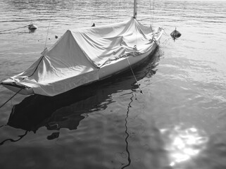 Black and white water landscape. White boat and boat water reflexion in water. Lake water surface. View of small sailboats floating on lake near pier. White boat in dock. Lake Garda, Italy.   - Powered by Adobe