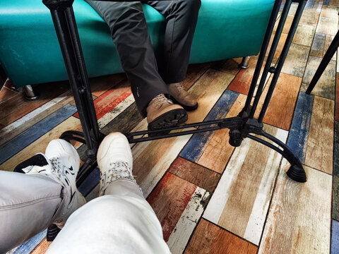 Legs of two seated people facing each other, focus on footwear. Two People Sitting Opposite Each Other in a cafe or restaurant Room With a Colorful Floor