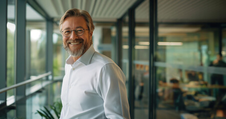 A likeable businessman stands in a modern office with glass walls and smiles into the camera - the topic is board of directors, career and success