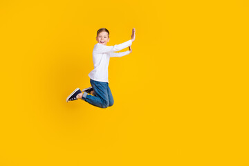 Full length photo of excited funky kid dressed white shirt jumping high pushing arms hands empty...