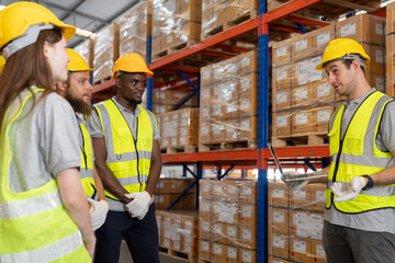 A warehouse worker matures logistics manager talking with a team of dispatchers in a meeting. Group of warehouse employees using a digital warehouse management system.