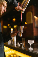 Professional barman pours shaken up cocktail before serving. Bartender prepares refreshing beverage for pouring into frozen stemmed glass