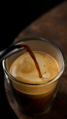 Pouring black coffee espresso with foam in glass