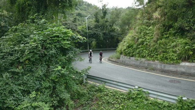 young asian couple cyclists riding bike on rural road, drone shot