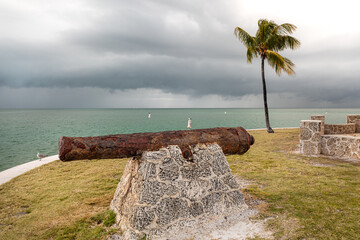 An old cannon rests on a stone base near a palm tree on Boca Chita, Florida

