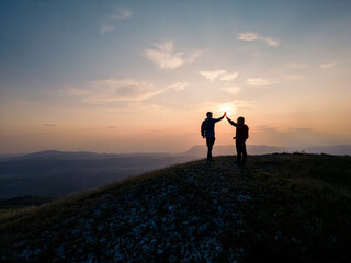 Teenage hiking adventure, a cheerful teen girl and a teen boy giving high five on the mountain top, enjoying success. Fun, inspiration, and recreation concepts.