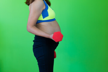 close up photo of pregnant woman belly lifting weights exercising. green background with copy space