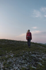 Obraz premium Female hiker silhouette with a backpack walking and following the trail uphill, enjoying the sky at sunset. Inspiration and healthy lifestyles concepts.