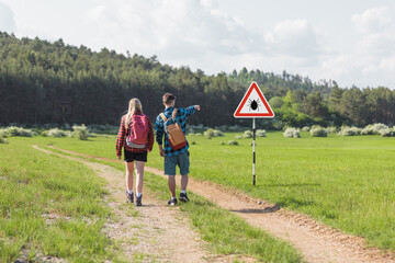 Hikers walking past tick Infected area with danger sign. Risk of tick-borne and lyme disease.