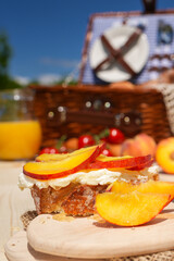 Picnic in the middle of nature. Folk scenery setup with a picnic basket on a wooden table. Fresh bread with cheese cream spread peaches and honey on top of it. Tasty desert.