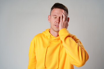 Portrait of young man in yellow hoodie with face palm gesture on gray background