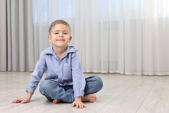 Cute little boy sitting on warm floor at home, space for text. Heating system