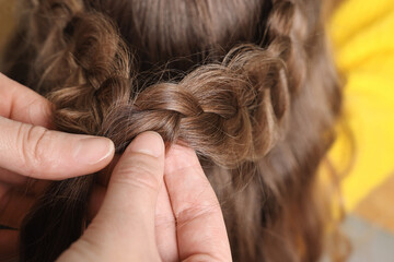 Professional stylist braiding girl's hair indoors, closeup