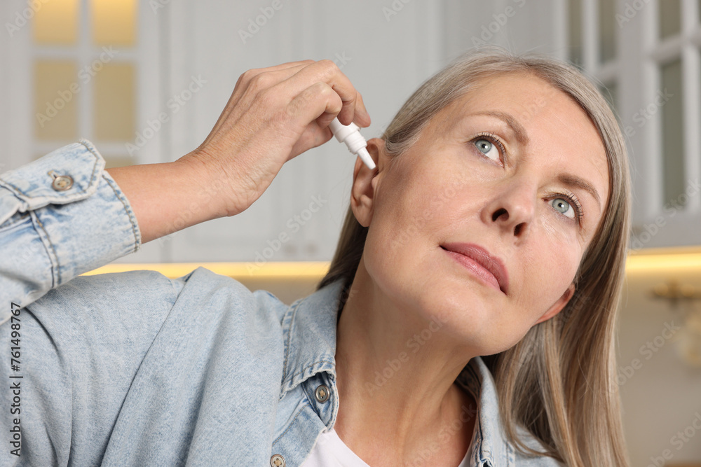 Wall mural Woman applying medical ear drops at home