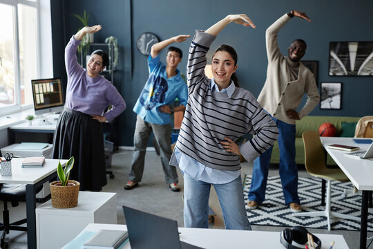 Diverse group of cheerful people enjoying stretching exercises in morning starting workday at office