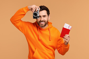 Smiling man with passport, camera and tickets on beige background