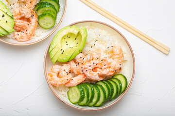 Two white ceramic bowls with rice, shrimps, avocado, vegetables and sesame seeds and wooden sticks...