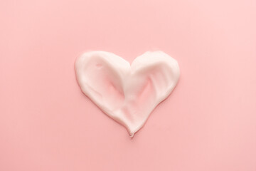 Heart shape skincare cream smear on pink background. Cosmetic lotion swatch texture of face cream,...
