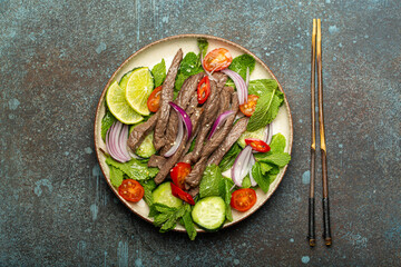 Plate with traditional Thai beef salad with vegetables and mint top view served on rustic concrete stone background, healthy exotic asian meal. - 761507555