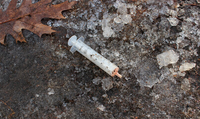 Dirty disposable syringe with blood residue inside on frozen ground