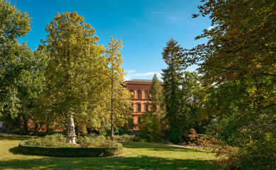 Die Fassade der  denkmalgeschützten ehemaligen "Gewerbe- und Bürgerschule" schimmert durch die Bäume am Rand des sommerlichen Lennéparks in Frankfurt (Oder)