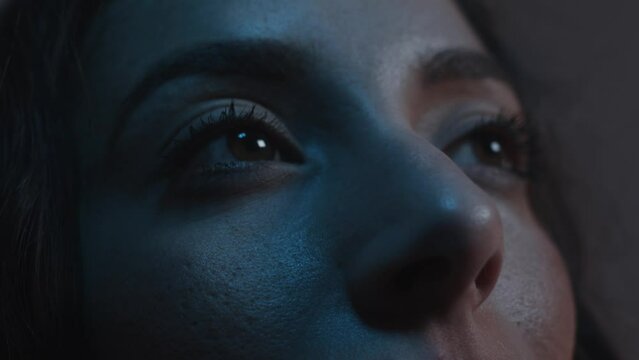 Close up on eyes looking up to a screen colours change on woman's face