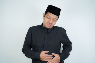 Asian Muslim man having stomach ache, bending over and holding hands on stomach, uncomfortable due...
