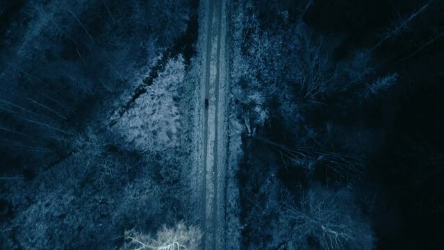 Top down aerial shot of lonely figure of cyclist ride on icy and snowy gravel road in the forest. Off road cyclist in winter outfit on snow covered rural road in the forest.
