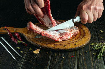 Chef uses a knife to remove meat from bones on a cutting board before preparing a dinner or...