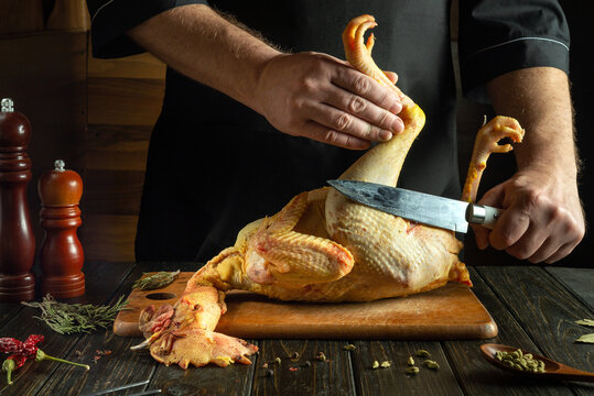 A chef tries to cut a raw rooster with a knife on a kitchen board. The concept of cooking curia with spices for a festive lunch. European cuisine.