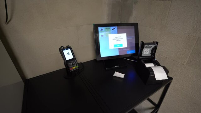 Cesis, Latvia - February 14, 2024 - A point-of-sale system on a black table, featuring a card payment terminal, a touchscreen monitor displaying a user interface, and an open thermal receipt printer 