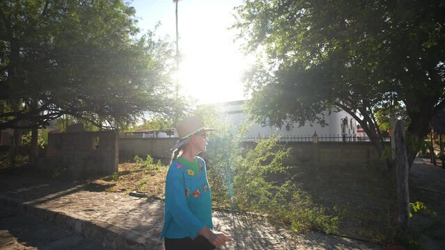 Mature woman tourist wearing straw hat and ethnic traditional clothes walking the streets of the historical mining town of El Triunfo, Mexico with setting sun.