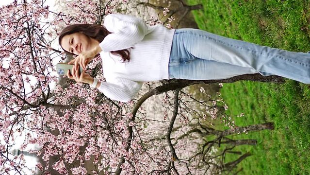 Lovely young woman taking photo of blooming pink and white garden Petrin in Prague, spring time in Europe