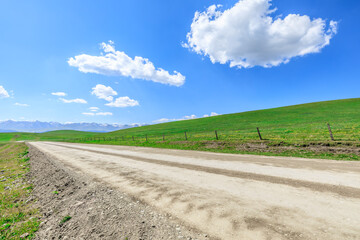 Dirt road and green meadow with mountain nature landscape on a sunny day