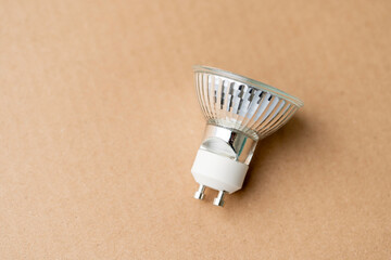 A small light bulb sits on a brown surface. The bulb is white and has a silver base.