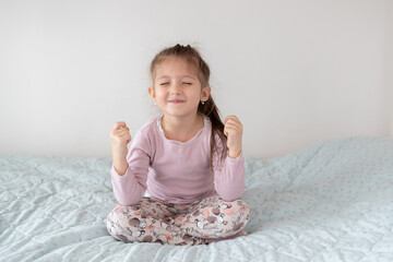 Funny kid doing yoga exercise at home. Little girl sitting in a yoga pose in bed - 761539179