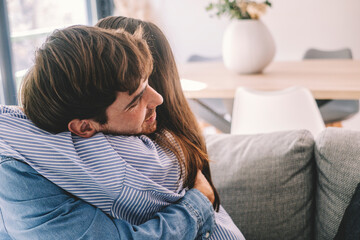 Smiling couple sitting on sofa at home hugging each other happy. Concept of love and happiness in...