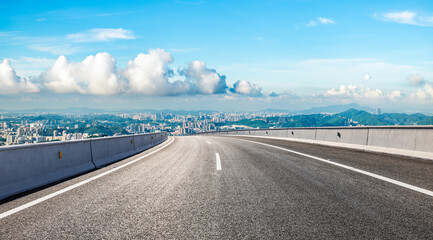 Asphalt highway road and city skyline with green mountain under blue sky