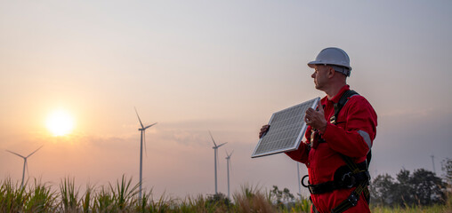 Engineers wearing uniform holding solar call panel work in wind turbine farms rotation to...