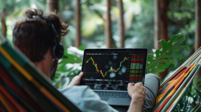 Successful rich stock trading investor, man trader or broker relaxing in hammock on nature using laptop computer investing money in rising financial market analyzing charts on screen. Over shoulder.