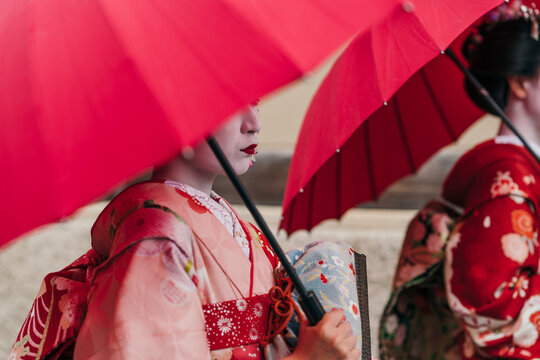 Two maiko geisha carries her red parasol with poise, her floral kimono a testament to the timeless beauty of Japanese cultural dress.