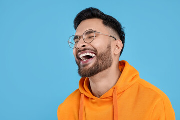 Handsome young man laughing on light blue background, space for text