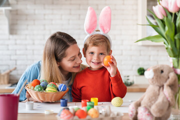 Little nice boy showing painted egg for Easter with his young mom at home. Small kid child son...