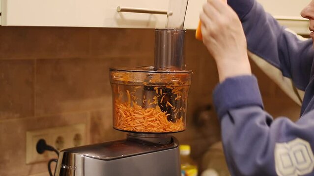 A woman is grinding carrots with a food processor.