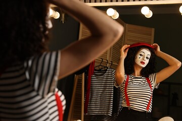 Young woman in mime costume putting beret near mirror indoors