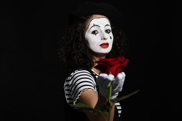 Fototapeta na wymiar Young woman in mime costume with red rose posing on black background